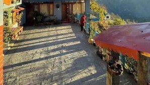 Ein traditionelles Gebäude mit rotem Dach, einer Holztreppe zum Eingang und einer Bergblick im Hintergrund.