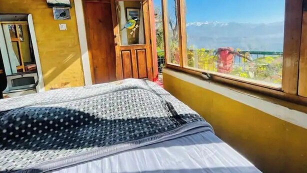 Ein Schlafzimmer mit einem Bett, einer Holztür, einem Fenster mit Bergblick und einem kleinen Tisch mit Stuhl.