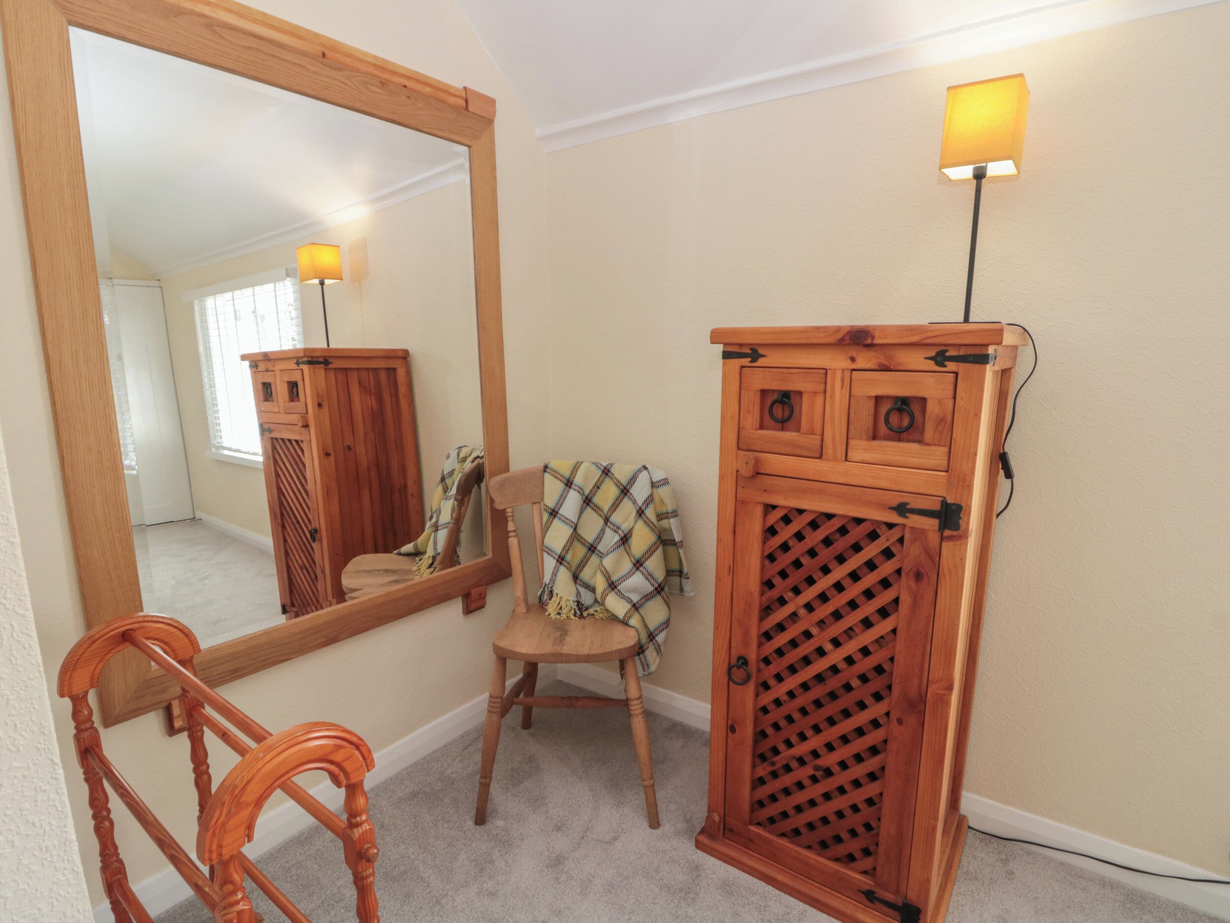 A room with a wooden chair, a wooden cabinet with a lattice design, and a mirror.