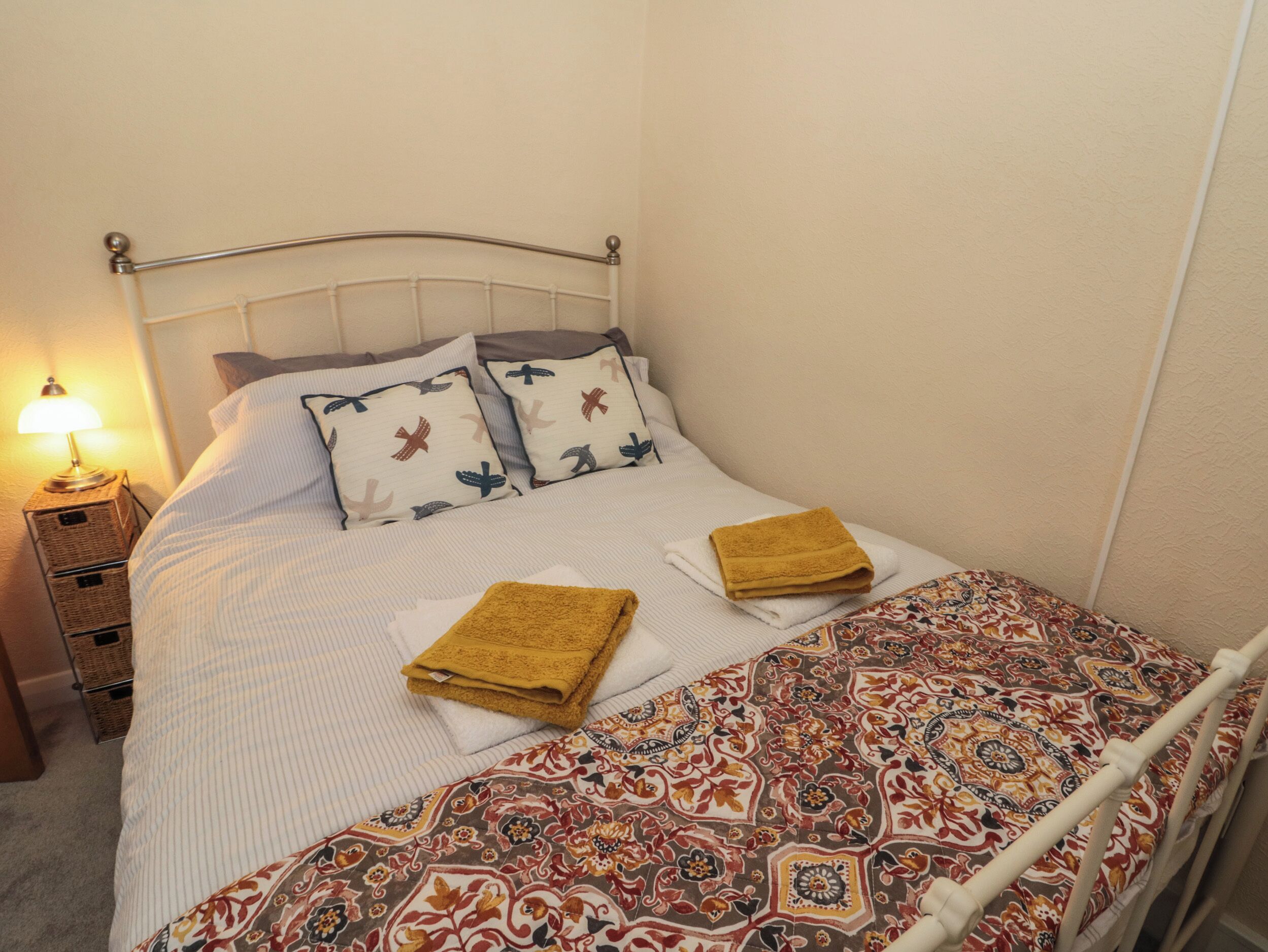 A neatly made bed with patterned bedding, a bedside lamp, and a small wooden nightstand.