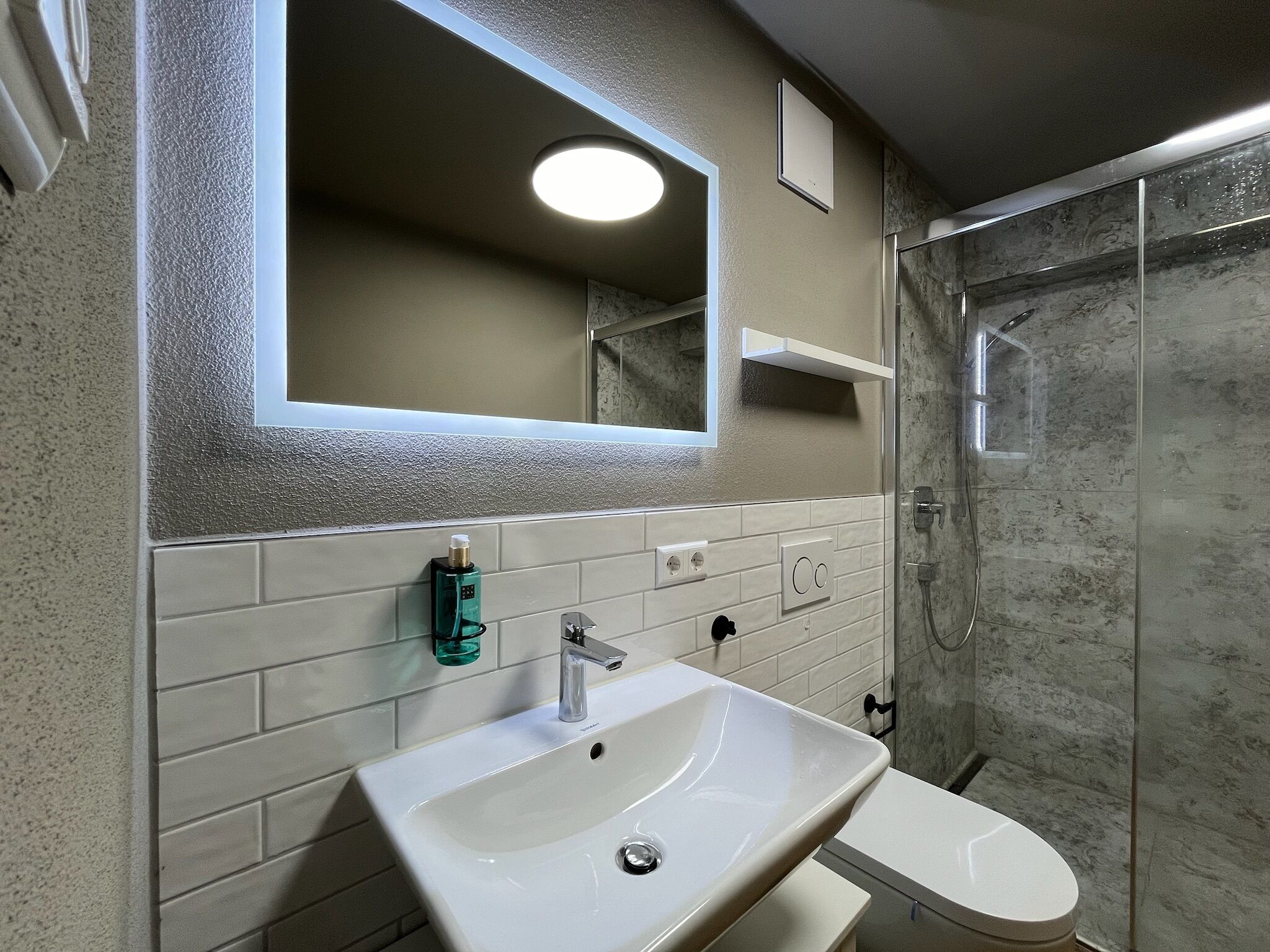 A bathroom with a white sink, a mirror, a toilet, and a shower area.