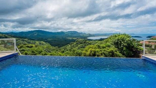 Ein Schwimmbecken mit Blick auf eine gebirgige Landschaft und ein Gewässer in der Ferne.
