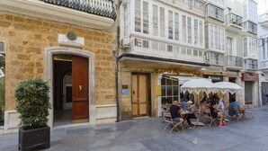 An outdoor cafe with tables and chairs, a stone building with a wooden door, and a sign above the door. - Estudio Amor BRUJO by Cadiz4Rentals (Cádiz)