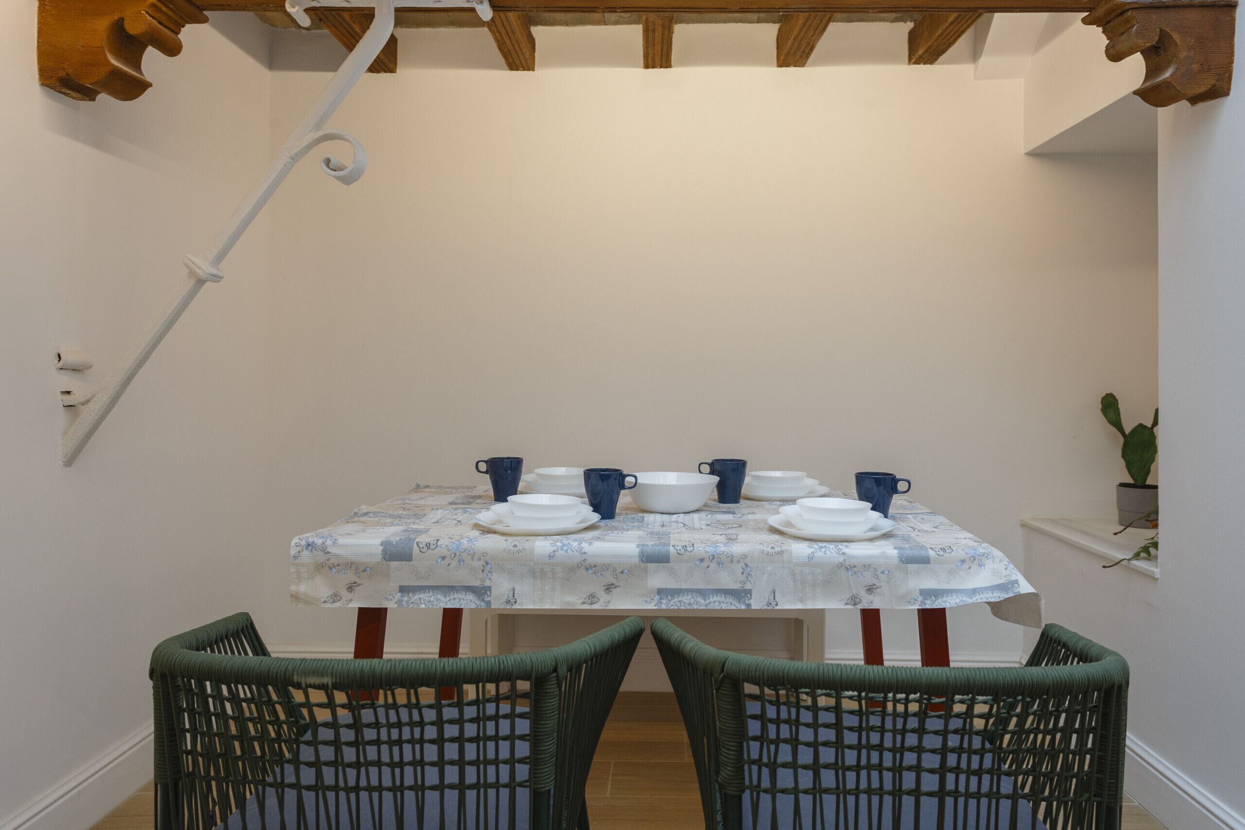 A dining area with a table set for four, surrounded by wicker chairs, under a wooden ceiling with exposed beams.