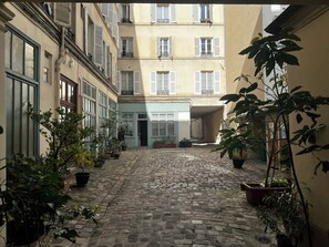 A cobblestone courtyard with potted plants and buildings with shutters.