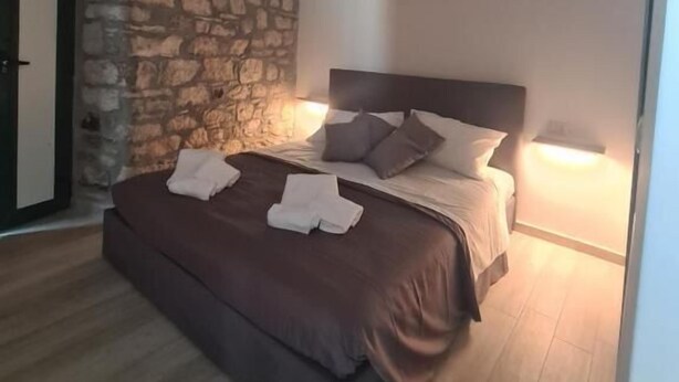 A bedroom with a stone wall, a bed with pillows and towels, and a wooden floor. - Il Campanile (Santa Maria del Molise)