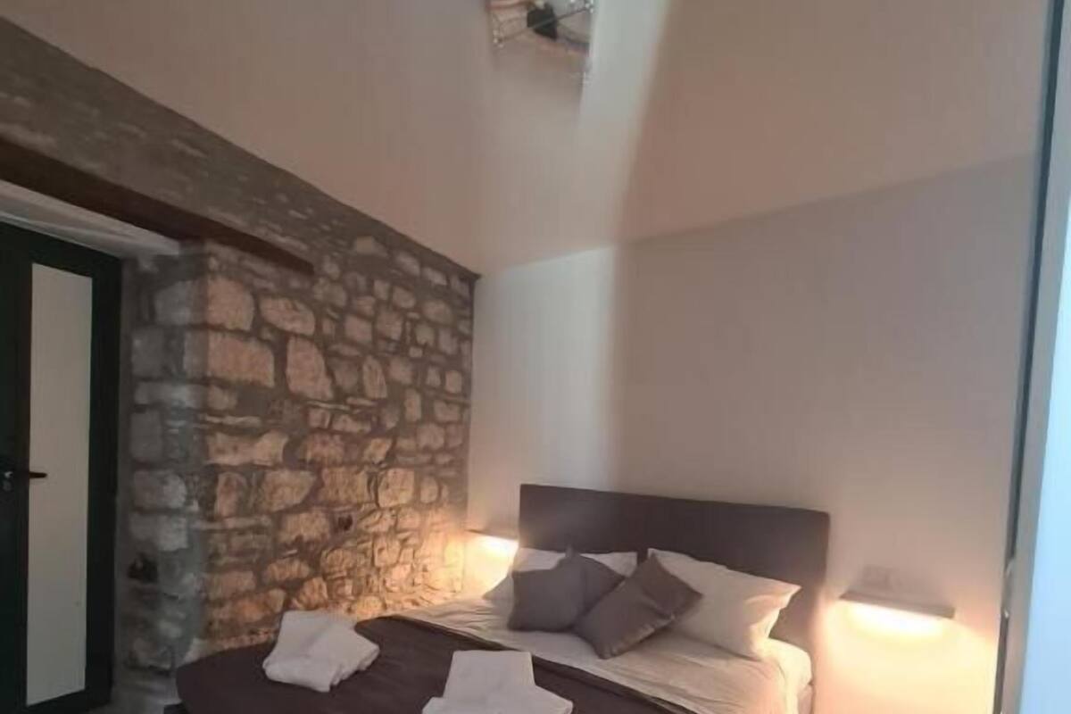 A bedroom with a stone wall, a bed with pillows and towels, and a wooden floor.