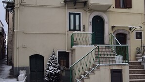 A multi-story building with a green door, a staircase with a green railing, and a snow-covered ground. - Il Campanile (Santa Maria del Molise)