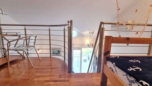 A loft-style bedroom with a wooden floor, a metal-framed chair, a bunk bed, and a view of the outdoors through a glass door. - Holiday apartment mit Klimaanlage und WLAN (Baška)