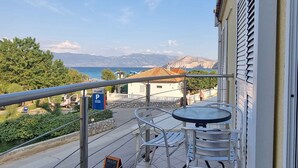 A balcony with a table and chairs, overlooking a coastal area with a restaurant and a parking sign. - Holiday apartment mit Klimaanlage und WLAN (Baška)