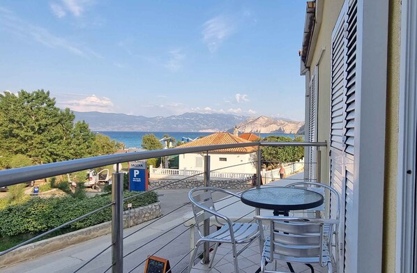 A balcony with a table and chairs, overlooking a coastal area with a restaurant and a parking sign.