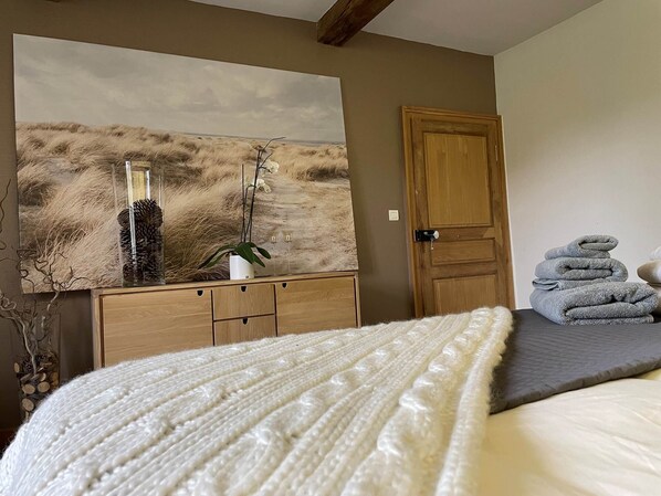 A bedroom with a bed, a wooden dresser, a large landscape painting, and a door.