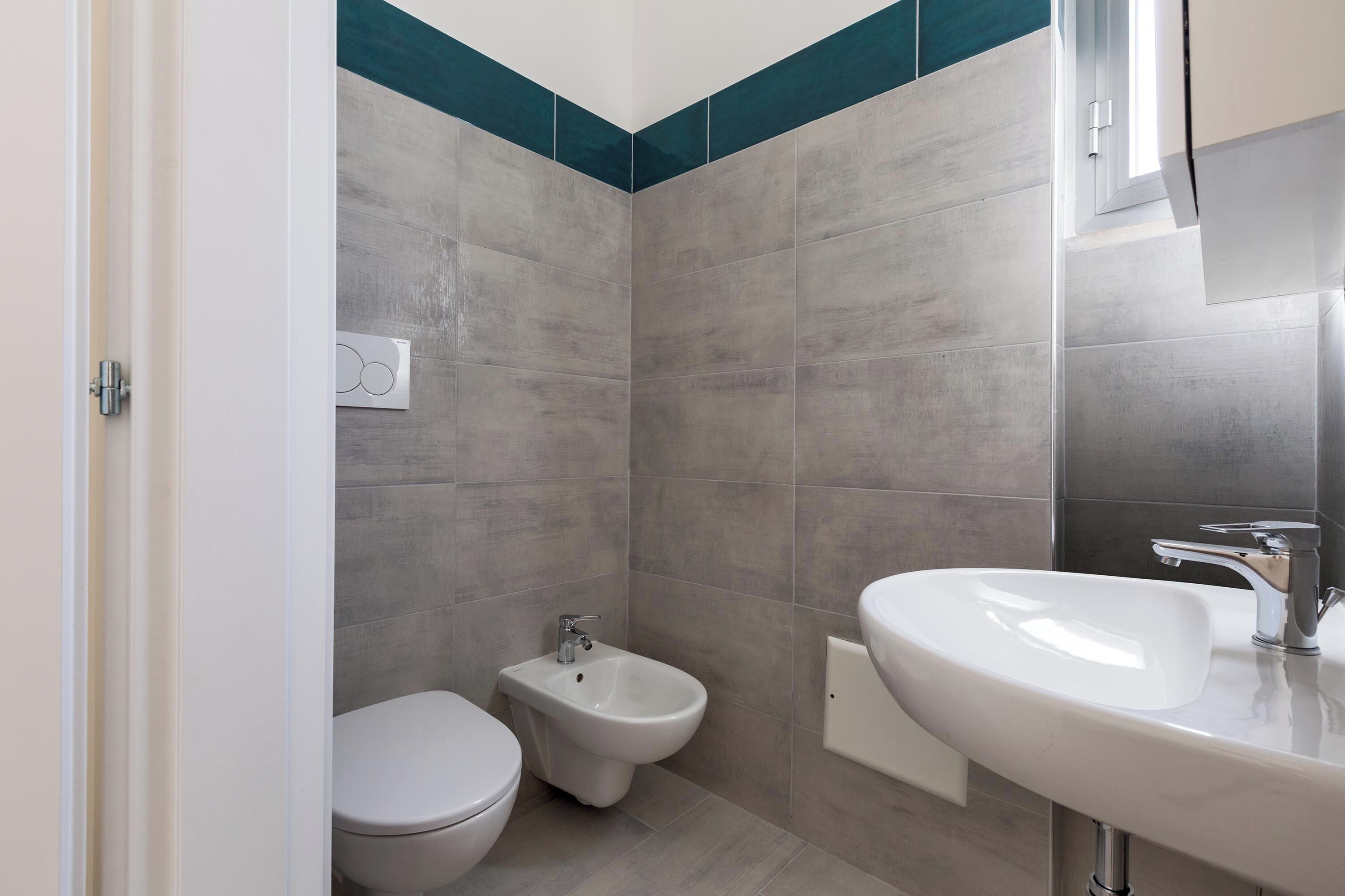A modern bathroom with grey tiles, a white sink, a bidet, and a toilet.