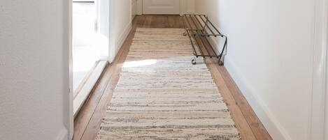 A hallway with a wooden floor, a white door, and a wall-mounted rack.