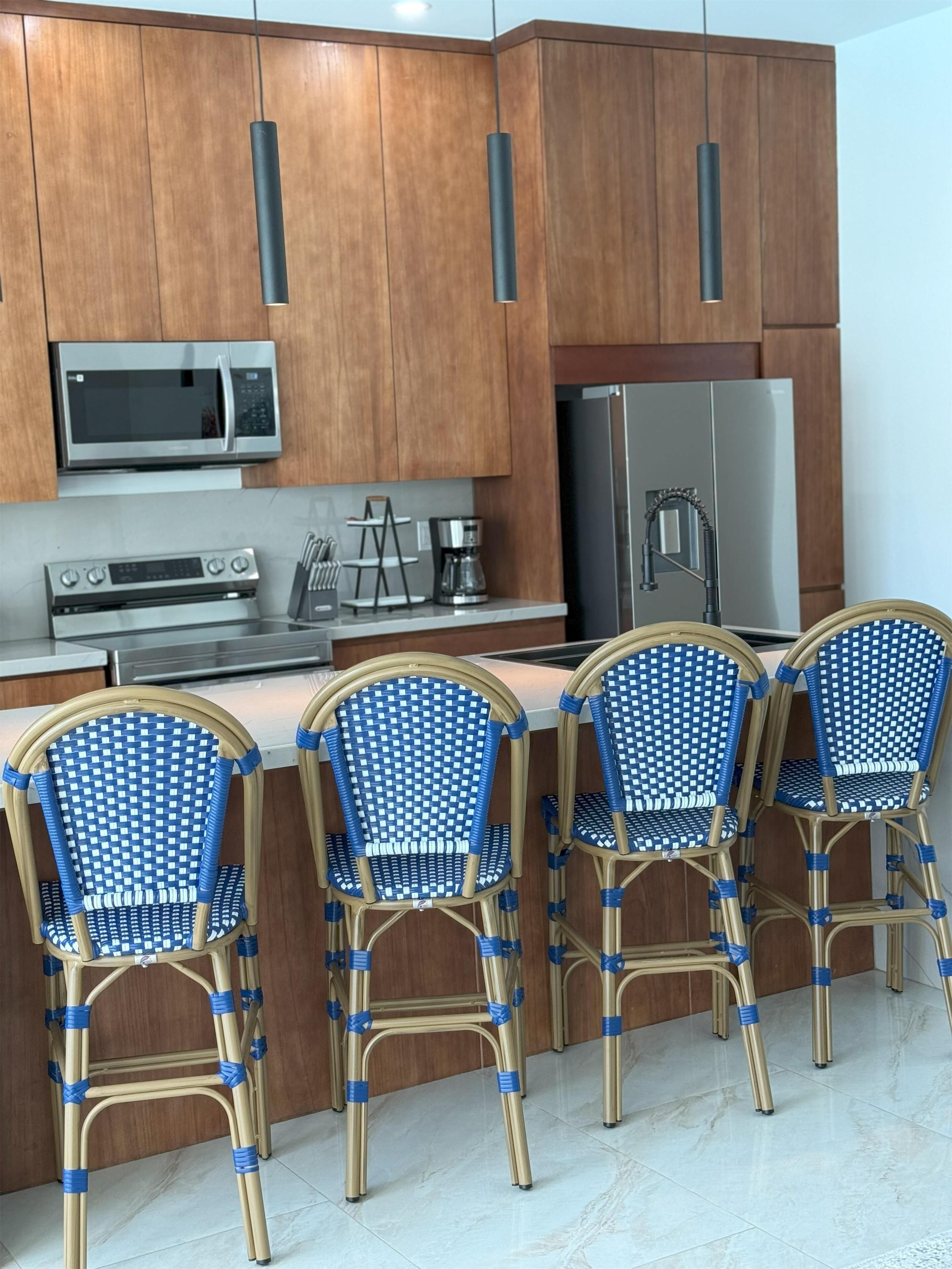 Une cuisine avec des meubles de rangement en bois, un four à micro-ondes, une cuisinière, un réfrigérateur et quatre chaises bleues et dorées.