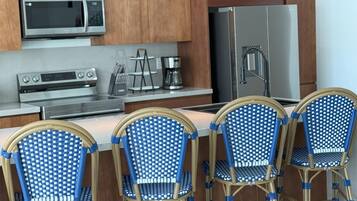 Une cuisine avec des meubles de rangement en bois, un four à micro-ondes, une cuisinière, un réfrigérateur et quatre chaises bleues et dorées.