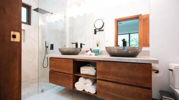 A modern bathroom with a glass shower enclosure, a wooden vanity with a large mirror, and a bowl sink.
