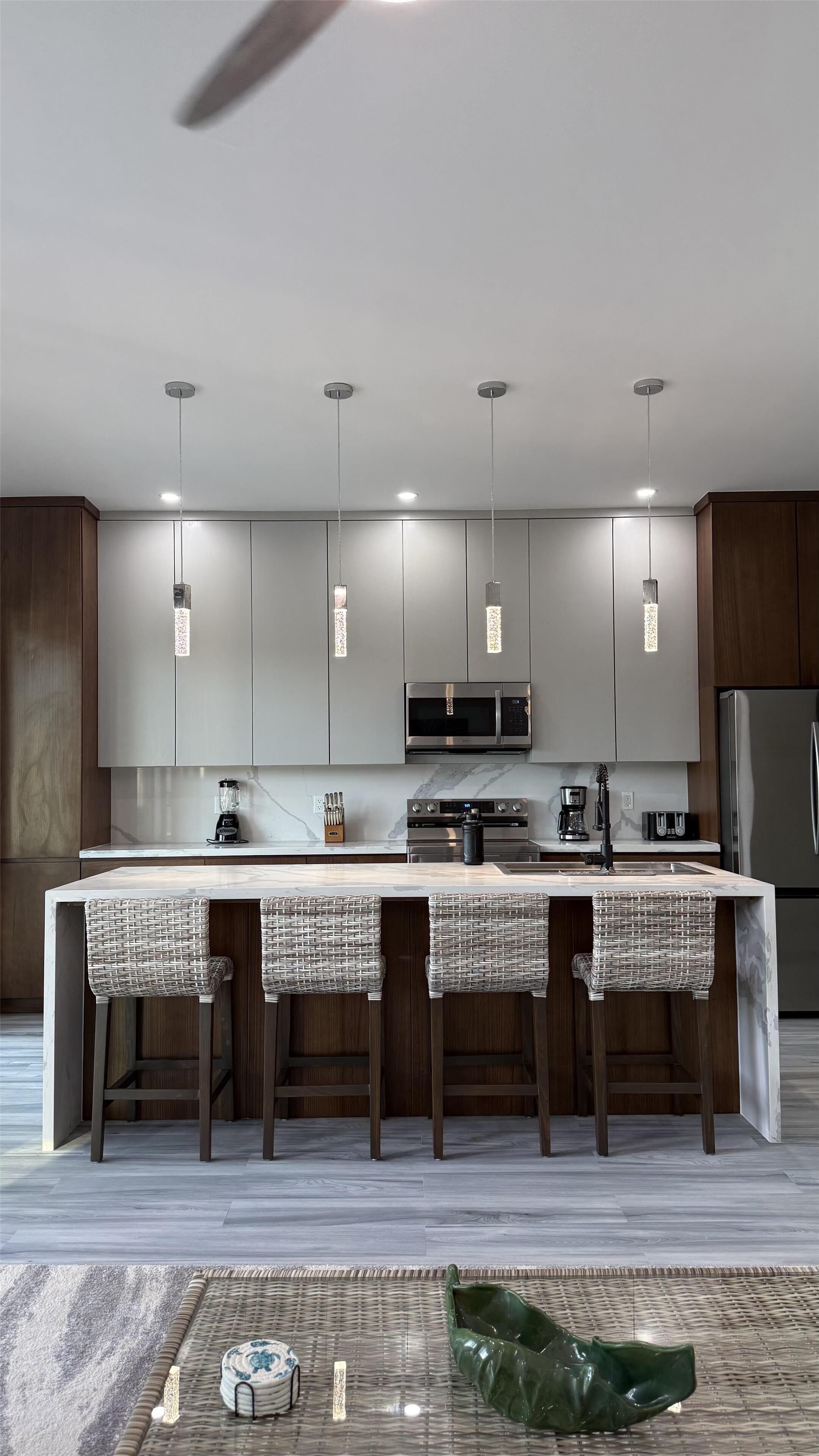 A modern kitchen with a central island, pendant lights, and stainless steel appliances.