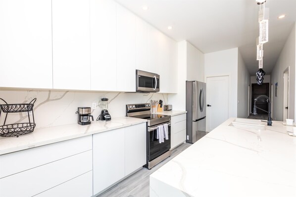 A modern kitchen with white cabinetry, stainless steel appliances, and a marble countertop. - Acqua Di Mare Resort (Roatan)