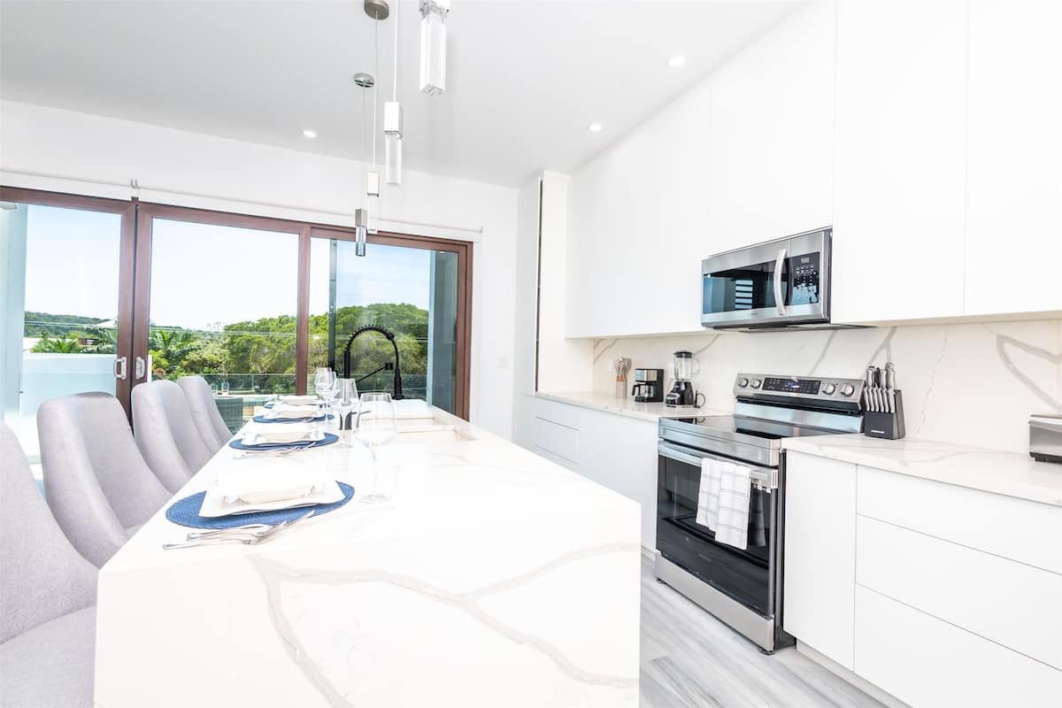 A modern kitchen with a large island, built-in oven, microwave, and a view of greenery outside.