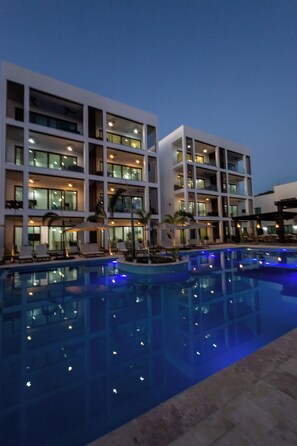 A modern hotel with multiple floors, a swimming pool with blue lighting, and outdoor seating areas. - Acqua Di Mare Resort (Roatan)