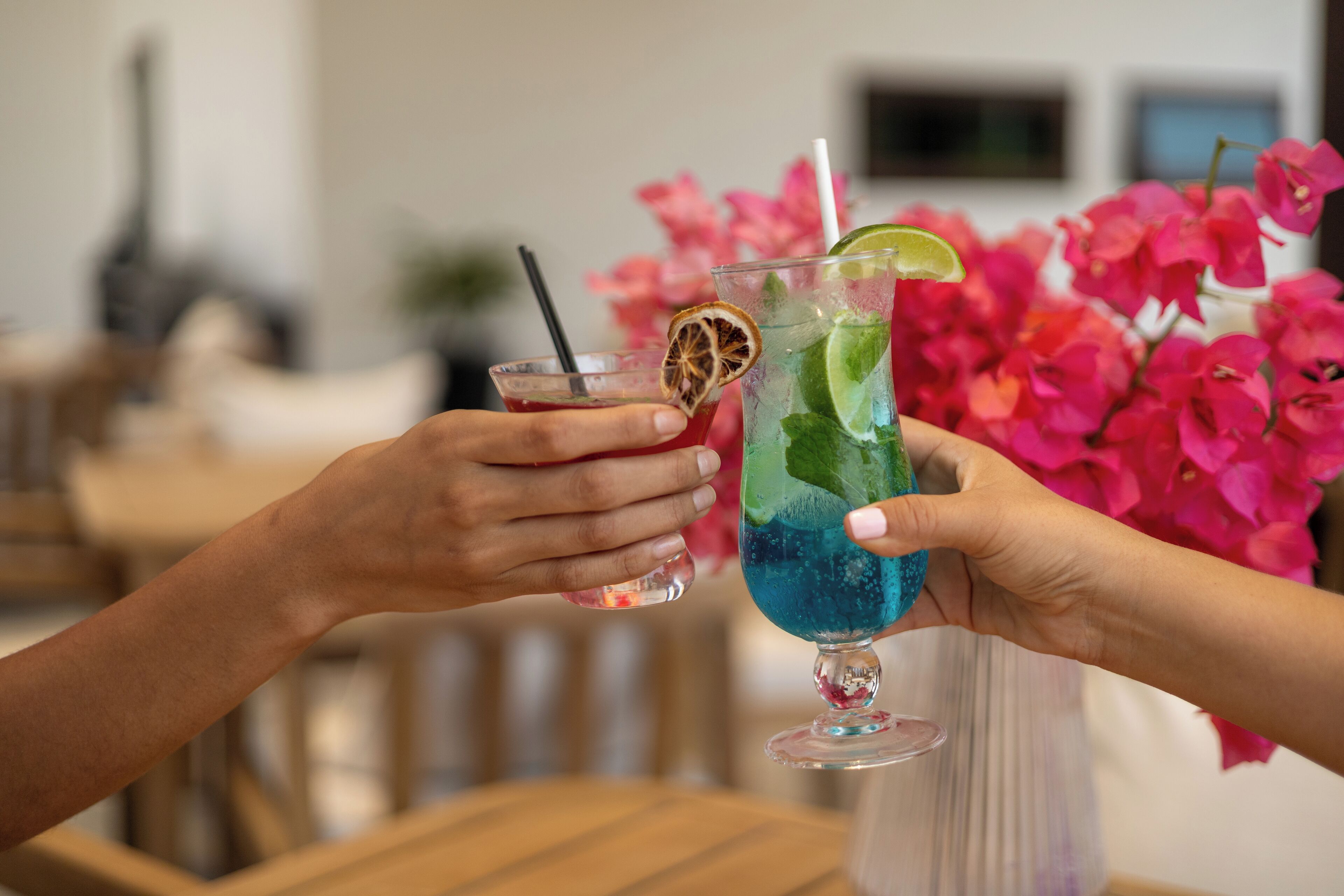 Two people holding cocktails with lime slices and straws.