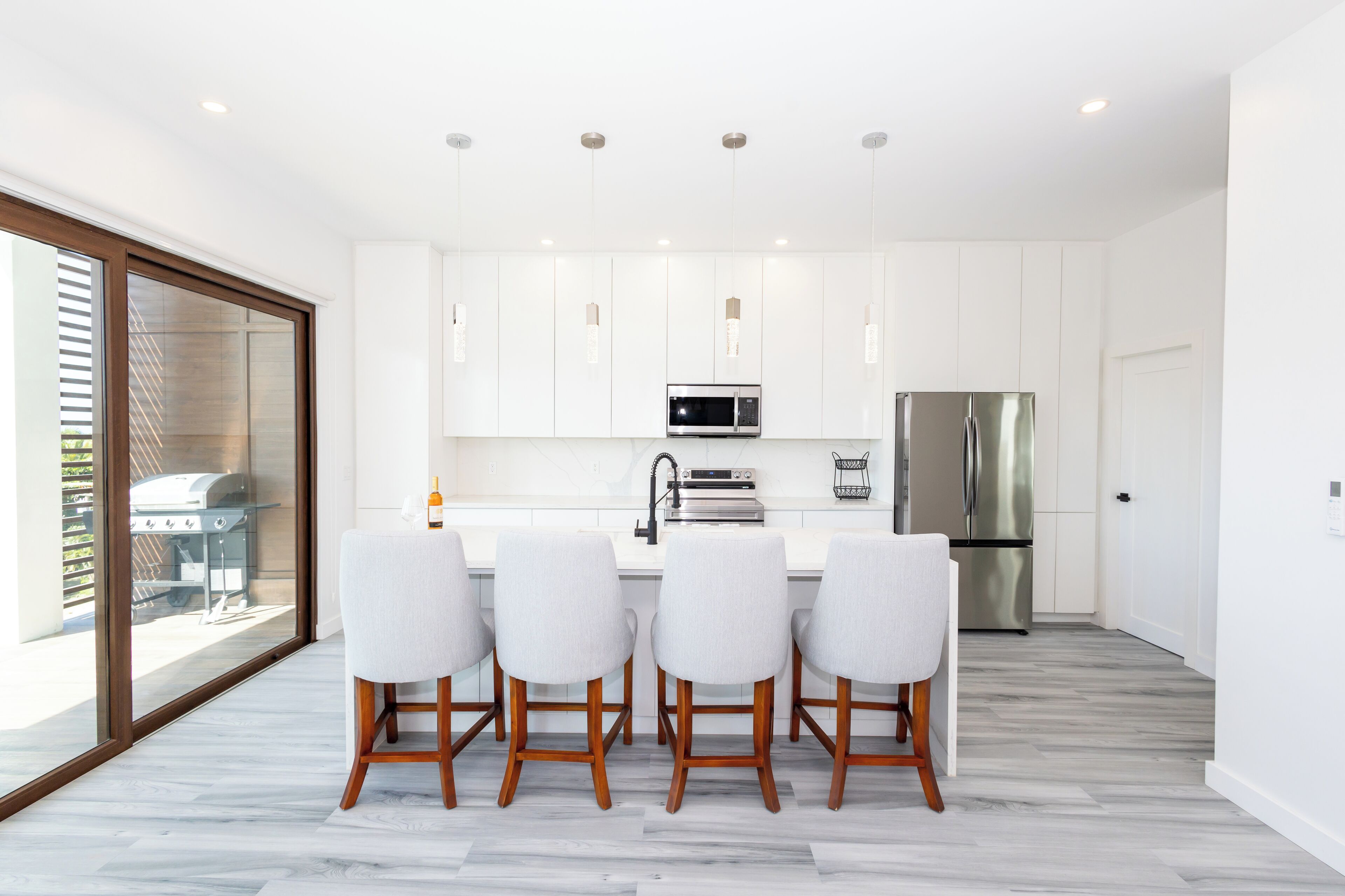 A modern kitchen with white cabinets, a stainless steel refrigerator, and a dining area with four chairs.