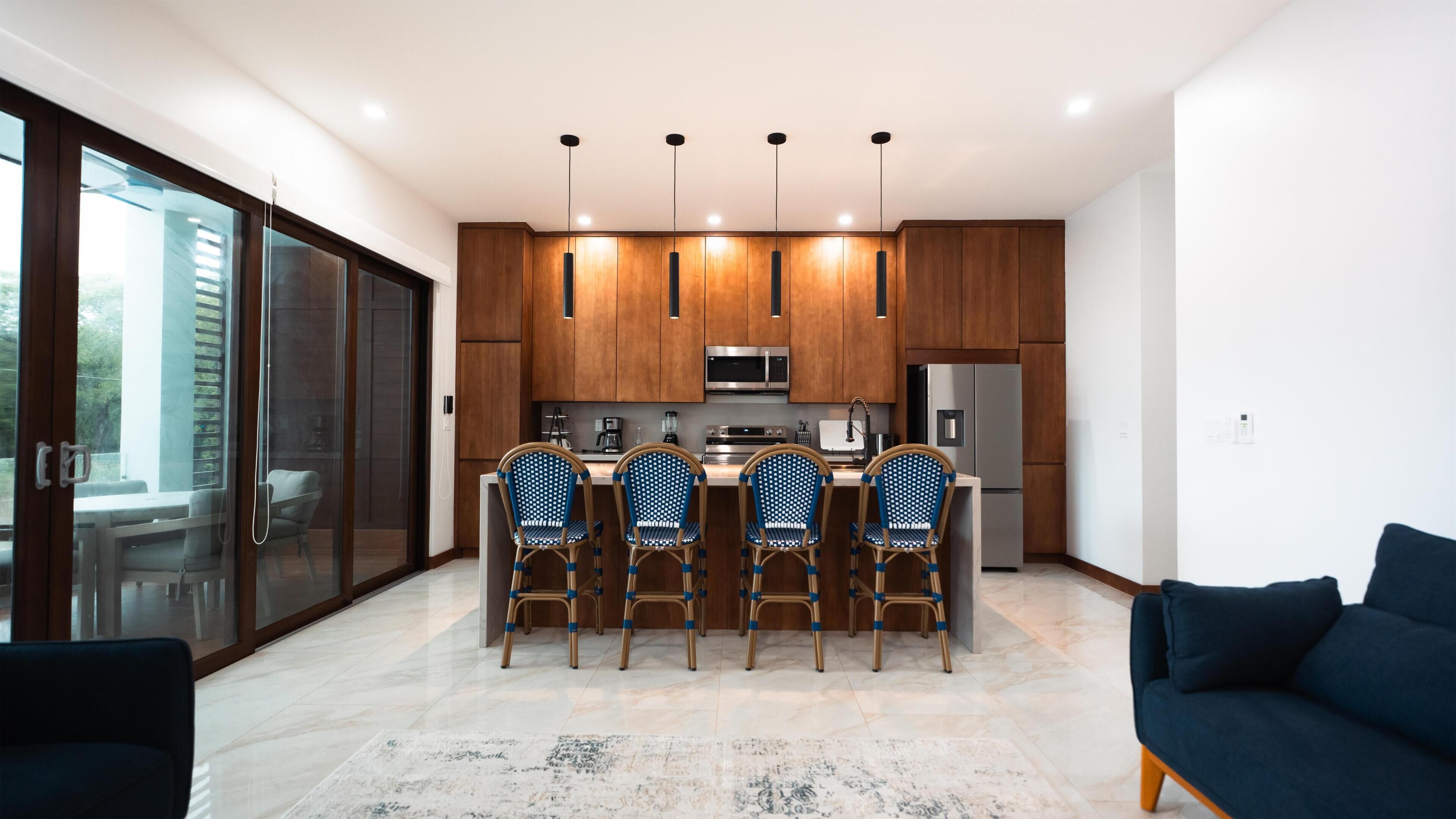 A modern kitchen with wooden cabinets, stainless steel appliances, and a bar area with four chairs.