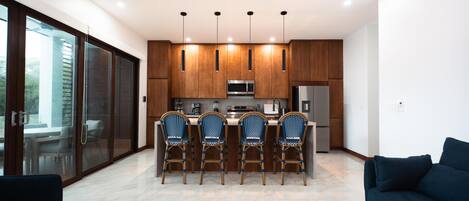 A modern kitchen with wooden cabinets, stainless steel appliances, and a bar area with four chairs.