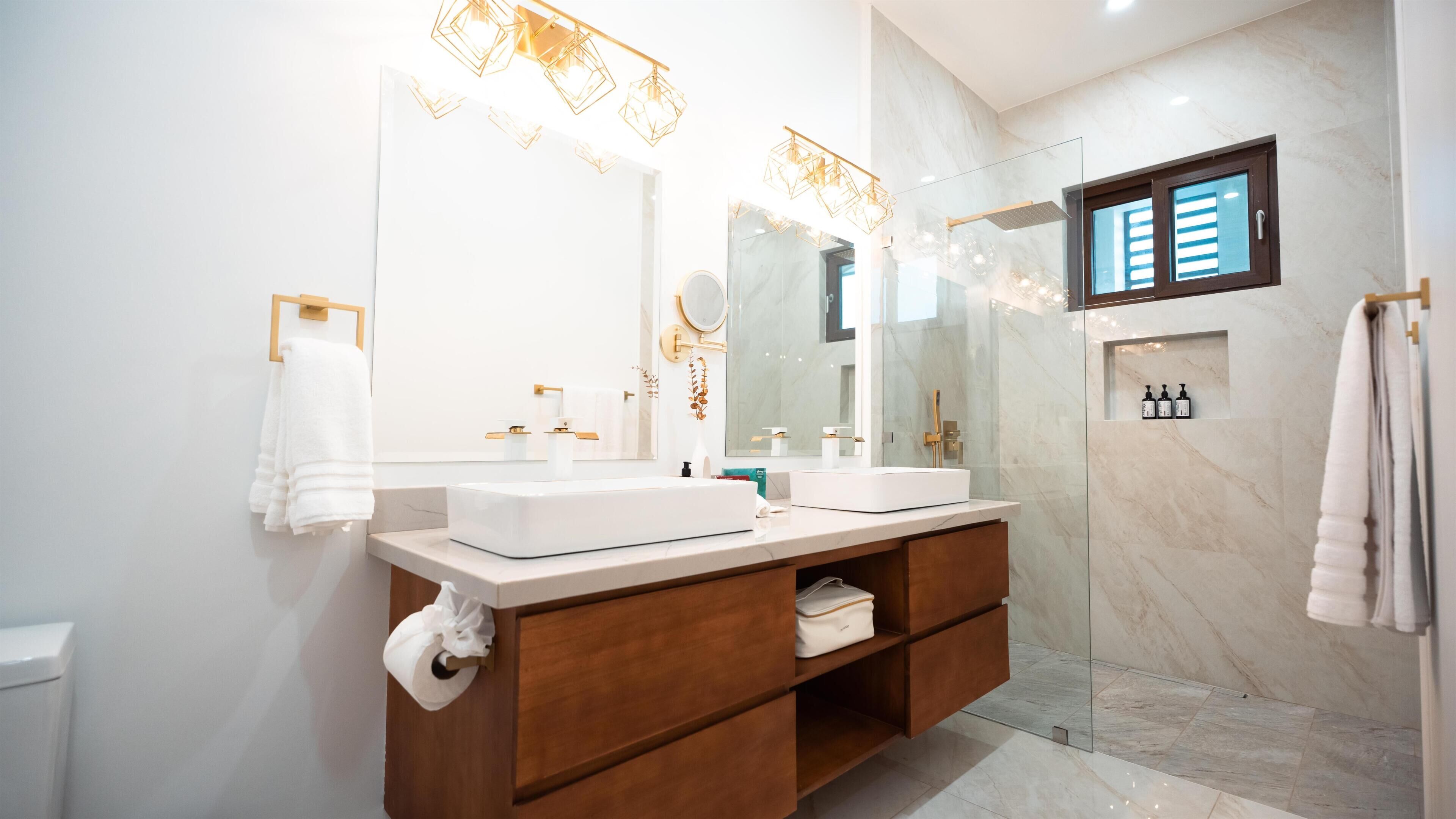 A modern bathroom with two sinks, a large mirror, a shower, and a towel rack.