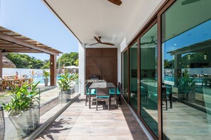 A modern outdoor patio with a dining table and chairs, a ceiling fan, and a glass-enclosed area with a pool view. - Acqua Di Mare Resort (Roatan)