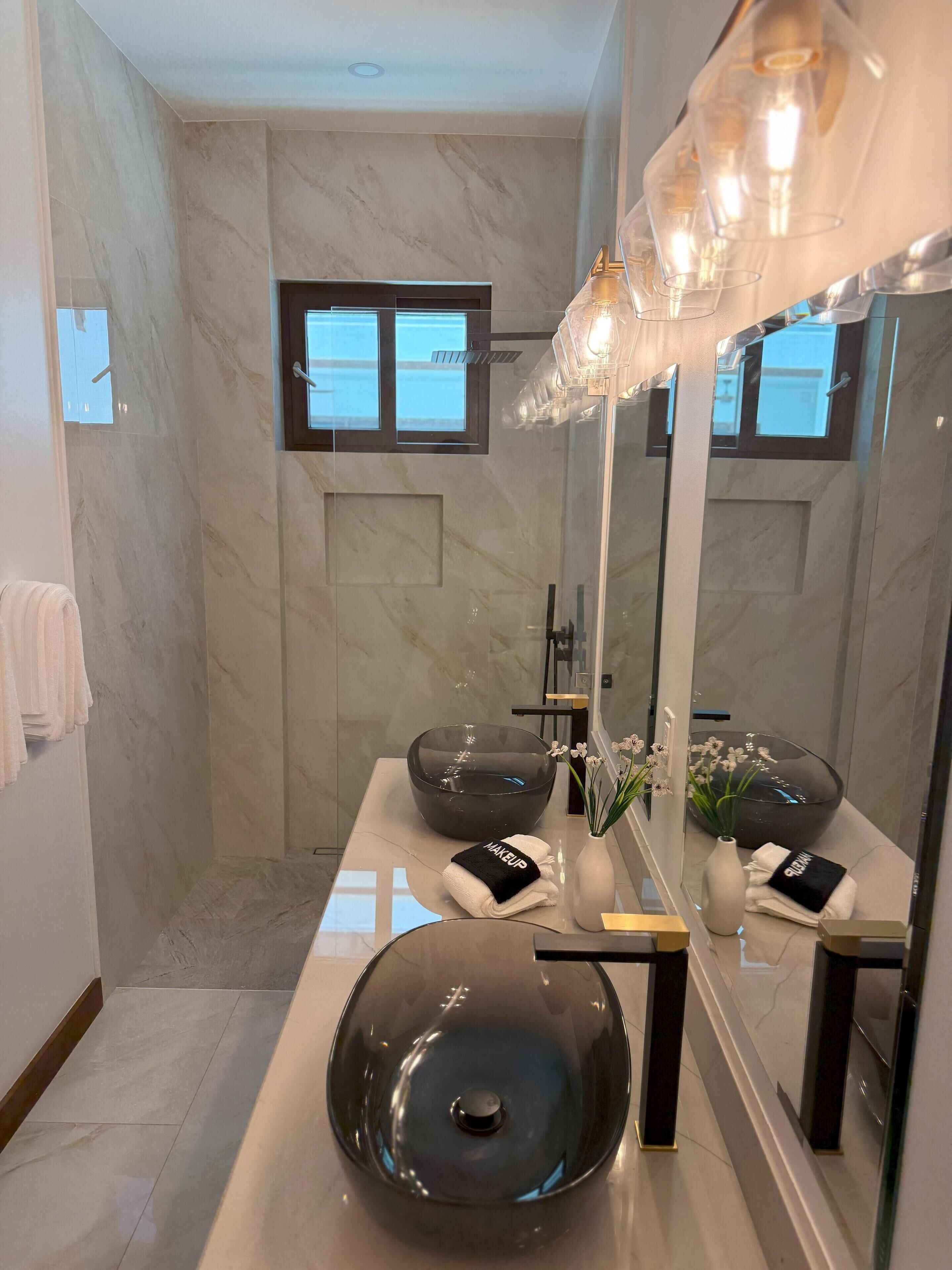 A modern bathroom with a large mirror, two bowls, a vase with flowers, and a towel rack.