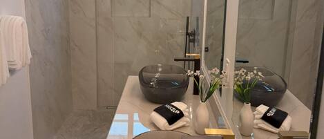 A modern bathroom with a large mirror, two bowls, a vase with flowers, and a towel rack.