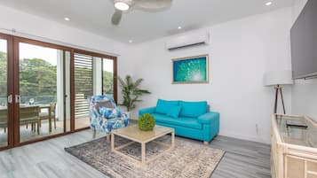 Una sala de estar moderna con un ventanal que da a un espacio exterior, un sofá azul, una mesa de centro de madera y un ventilador de techo.