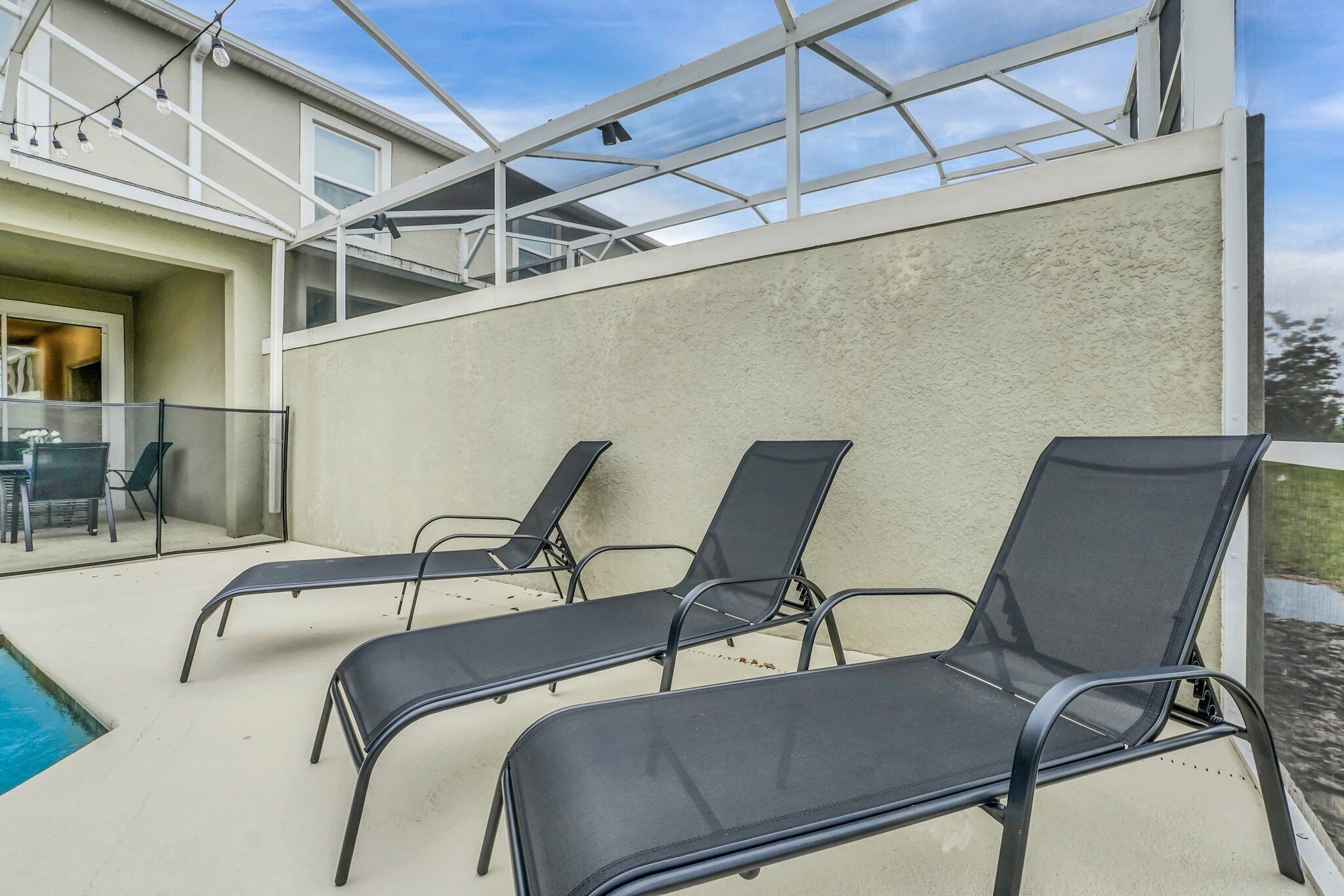 A rooftop terrace with three black lounge chairs, a glass table, and a pool.