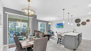 Una cocina moderna con una isla central, un comedor con una mesa grande y sillas, y vistas a un patio exterior a través de una puerta corrediza de vidrio.