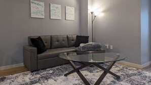 Een moderne woonkamer met een grijze bank, een glazen salontafel en abstracte wanddecoratie.