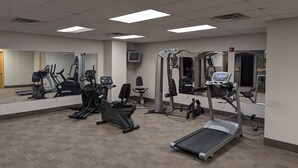 Een fitnessruimte met diverse trainingsapparaten, waaronder loopbanden, hometrainers en krachtapparaten.