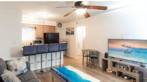 A modern living room with a sofa, a coffee table, a TV, and a ceiling fan. - Cozy beach cottage steps away from Hollywood Beach (Hollywood)