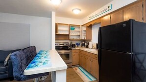 A compact kitchen with wooden cabinets, a black refrigerator, a dining table with a blue and white tablecloth, and a sofa. - Cozy beach cottage steps away from Hollywood Beach (Hollywood)