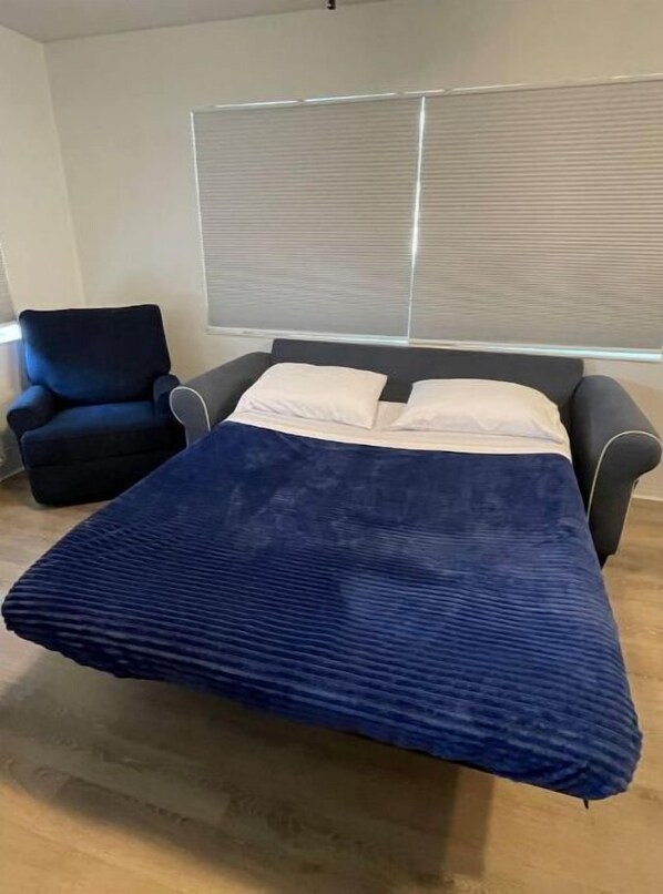 Una habitación con cama, una silla y ventana con persianas.
