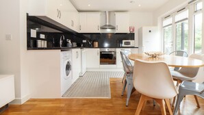 A modern kitchen with white cabinets, a black countertop, and a dining area with a round table and chairs. - Garras (Truro)