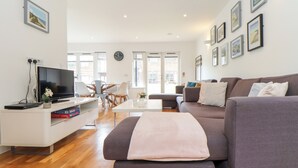 A modern living room with a flat-screen TV, a sofa, a coffee table, and a dining area with chairs. - Garras (Truro)