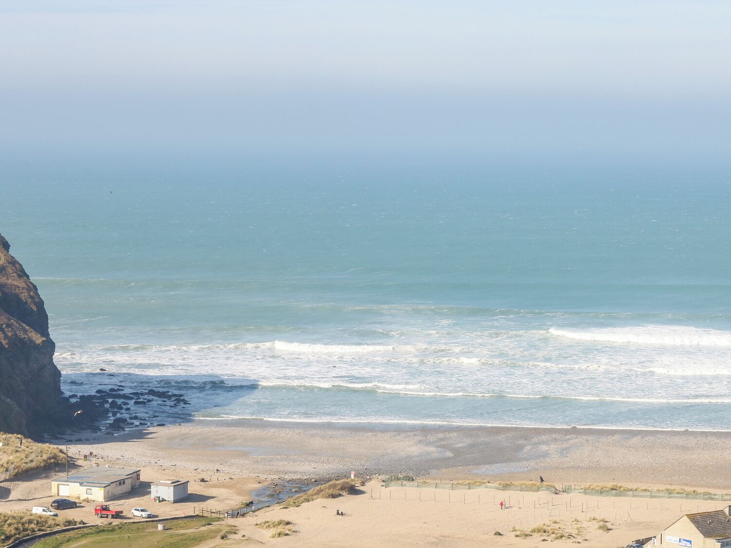 A coastal view with a beach, rocky cliffs, and a few buildings.