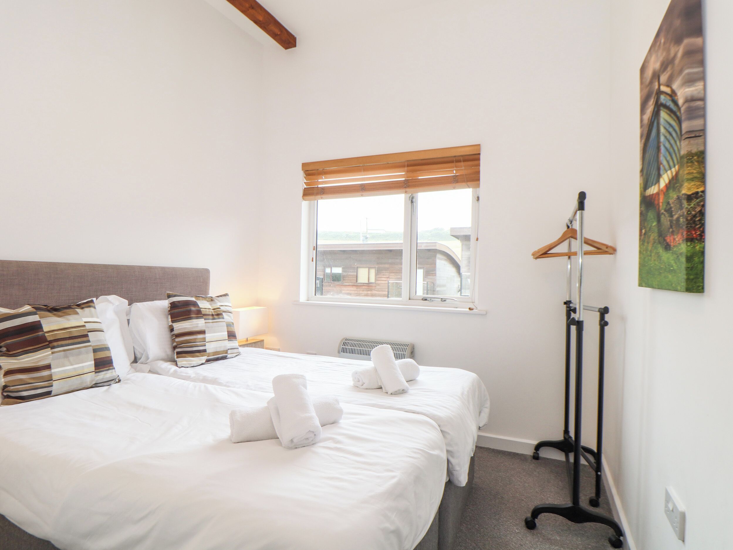 A hotel room with two beds, a window with blinds, a radiator, a coat rack, and a painting on the wall.