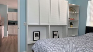 Camera da letto con un letto, un'armadio bianco e una piccola angolo cottura sullo sfondo.