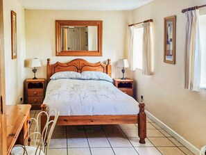 A bedroom with a wooden bed, two bedside tables with lamps, a mirror above the bed, and a window with curtains. - 2 bedroom accommodation in Bramerton (Bramerton)