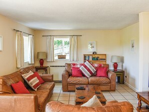 A living room with two brown leather sofas, a wooden coffee table, a bookshelf, and a window with curtains. - 2 bedroom accommodation in Bramerton (Bramerton)