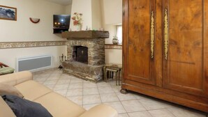 A living room with a stone fireplace, a television, a wooden cabinet, and a beige sofa. - Emeraude by Interhome (Saint Coulomb)