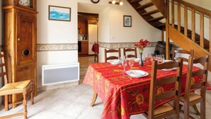 A dining area with a red tablecloth, wooden chairs, a clock, and a staircase. - Emeraude by Interhome (Saint Coulomb)